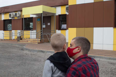 Dad takes his son to the doctor. Against the backdrop of a standard hospital building, father and son prepare for an examination. Concept of a single parent preparing child for school or kindergartenの写真素材