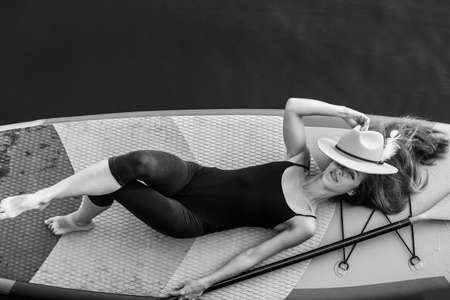 Close-up of a girl floating on a sup board. The concept of water sports, relaxation and self-immersion. Lonely woman alone on a board against a background of water and a pier.の写真素材