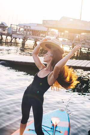 Close-up of a girl floating on a sup board. The concept of water sports, relaxation and self-immersion. Lonely woman alone on a board against a background of water and a pier.の写真素材