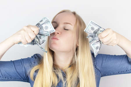 Close-up of a girl sniffing money. Madness and greed from currency. The concept of corruption and getting money at any cost. Squeeze and toss US dollars. Wild thirst for profitの写真素材