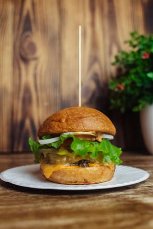 Close-up of a standard burger. Adult fast food in a restaurant or cafe. Macro photo of burger ingredients with meat, cheese and herbs. Eco burgers for the whole familyの写真素材