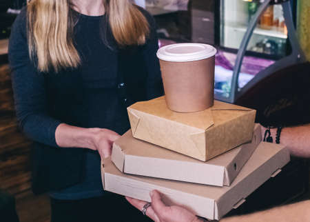 Food delivery. The girl holds paper bags with fast food in her hands. The concept of countering covid 19. Delivery from a restaurant or cafe. Unpacking meal containersの写真素材