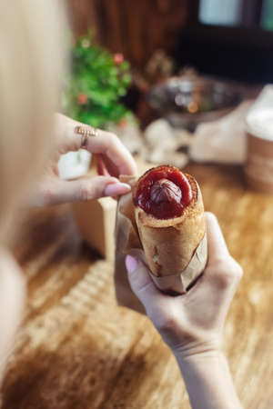 Close-up of a hot dog in hand. The girl has a French manicure. There is a lot of ketchup on top and...