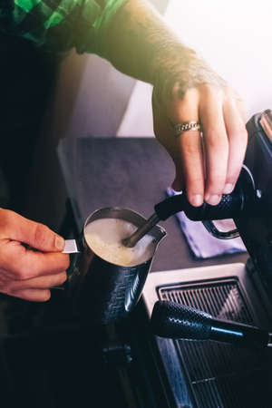 Close-up of a barista preparing coffee. The process of making cappuccino in a coffee machine. Measuring cup in hand. The hot drink is poured into a paper cup. Takeaway foodの写真素材