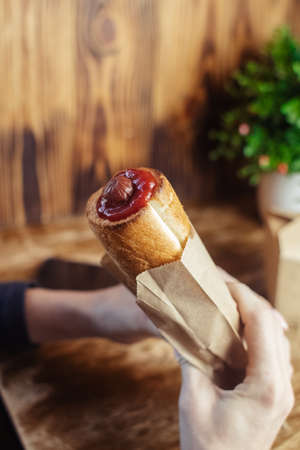 Close-up of a hot dog in hand. The girl has a French manicure. There is a lot of ketchup on top and...