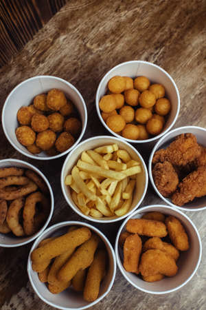 Top view of onion rings, cheese balls, chicken nuggets, wings in batter, fries and cheese sticks. Six-course set in paper buckets. Fast food cafes and restaurants. Food is laid out in shape of flowerの写真素材
