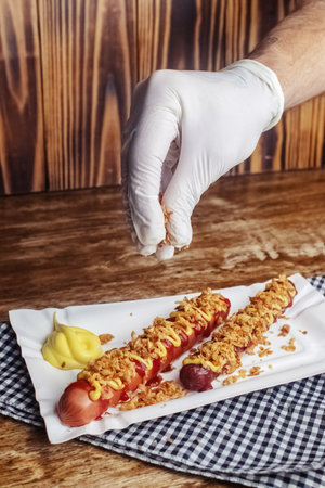 Grilled sausages closeup. The meat dish is sprinkled with dried caramelized onions. Top with grated cheese, mustard and ketchup. Isolated on a wooden background. Fast food in cafes and restaurantsの写真素材
