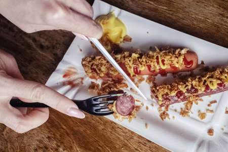 Grilled sausages closeup. The meat dish is sprinkled with dried caramelized onions. Top with grated cheese, mustard and ketchup. Isolated on a wooden background. Fast food in cafes and restaurantsの写真素材