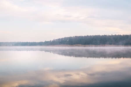 Background. Mountain lake in the fog. Magic morning. Fog spreads beautifully over the water surface. The trees are almost invisible. Clouds and sky are reflected from the surfaceの写真素材