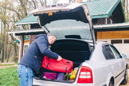 Close-up of a man who arrived at a country house in the woods. The head of the family takes bags from the trunk of the car. The concept of a rich holiday in a villa.の写真素材