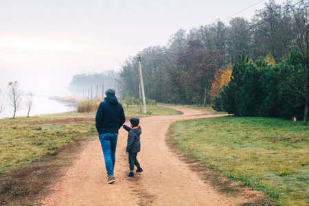 Dad and son in forest. Family vacation among the autumn trees. Walk along a dirt road near the forest and a country house. The concept of having a pleasant time with your father and a happy childhoodの写真素材