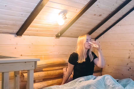 A beautiful girl lies on a bed in a room of a country house. Cozy wooden furniture creates comfort and coziness. Bare legs give a hint of eroticism.の写真素材