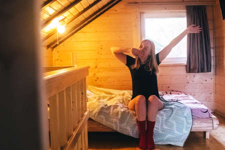 A beautiful girl lies on a bed in a room of a country house. Cozy wooden furniture creates comfort and coziness. Bare legs give a hint of eroticism.の写真素材