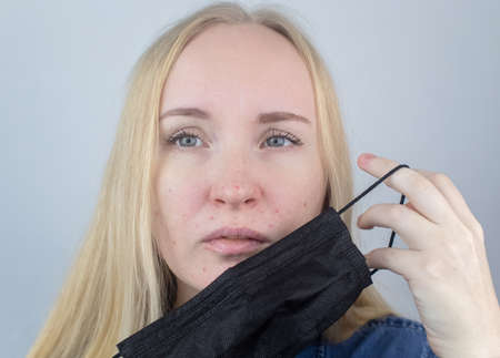 Woman removes the protective mask and shows irritation on face skin. Antiviral measures. Means of protection . Long wearing of a mask. Acne on face and chafing. Dry lips and red dotsの写真素材