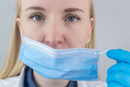 Doctor removes the protective mask and shows irritation on face skin. Antiviral measures. Means of protectionの写真素材