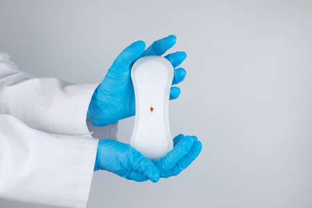 Hypomenorrhea. The woman shows a gynecological pad with a small drop of blood on it. Concept of small amounts during scanty menstruation. Complaints of pain and strange cycle. Diseases in gynecologyの写真素材