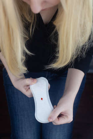 Hypomenorrhea. The woman shows a gynecological pad with a small drop of blood on it. Concept of small amounts during scanty menstruation. Complaints of pain and strange cycle. Diseases in gynecologyの写真素材