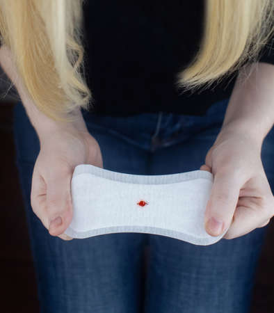 Hypomenorrhea. The woman shows a gynecological pad with a small drop of blood on it. Concept of small amounts during scanty menstruation. Complaints of pain and strange cycle. Diseases in gynecologyの写真素材