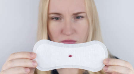Hypomenorrhea. The woman shows a gynecological pad with a small drop of blood on it. Concept of small amounts during scanty menstruation. Complaints of pain and strange cycle. Diseases in gynecologyの写真素材