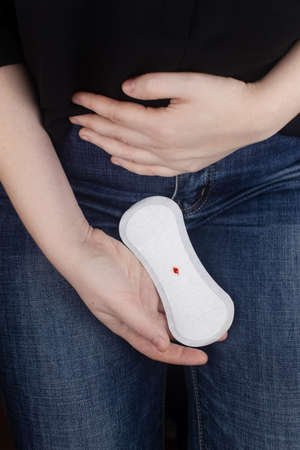 Hypomenorrhea. The woman shows a gynecological pad with a small drop of blood on it. Concept of small amounts during scanty menstruation. Complaints of pain and strange cycle. Diseases in gynecologyの写真素材