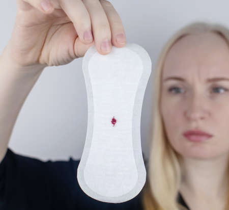 Hypomenorrhea. The woman shows a gynecological pad with a small drop of blood on it. Concept of small amounts during scanty menstruation. Complaints of pain and strange cycle. Diseases in gynecologyの写真素材
