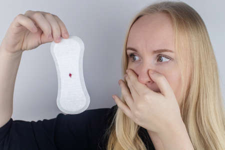 Hypomenorrhea. The woman shows a gynecological pad with a small drop of blood on it. Concept of small amounts during scanty menstruation. Complaints of pain and strange cycle. Diseases in gynecologyの写真素材