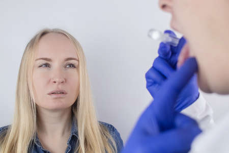 Clean tongue. The doctor teaches the patient how to clean the tongue properly. Dentist consultation. The blonde girl is trained in proper oral hygiene. Man and woman isolated on white backgroundの写真素材