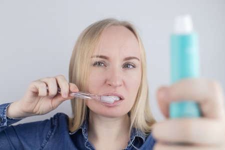 Close-up of a girl brushing teeth and look in front of a mirror. Oral hygiene. In the hands of objects for cleaning the oral cavity: a toothbrush and paste. Isolated on white background.の写真素材