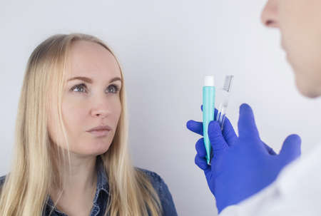 The dentist advises the girl on how to brush her teeth properly. The doctor teaches and explains. Isolated on white background. In the hands of a toothbrush and paste.の写真素材