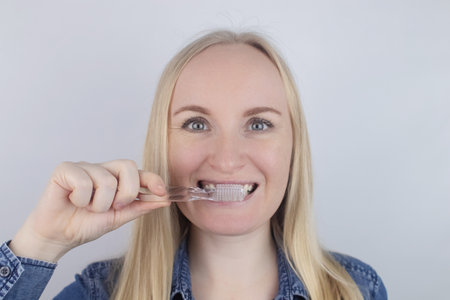 Close-up of a girl brushing teeth and look in front of a mirror. Oral hygiene. In the hands of objects for cleaning the oral cavity: a toothbrush and paste. Isolated on white background.の写真素材