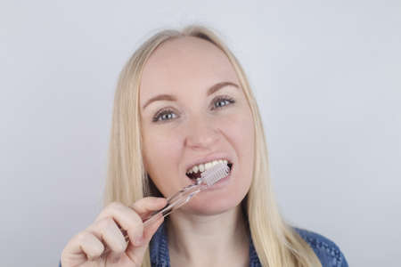 Close-up of a girl brushing teeth and look in front of a mirror. Oral hygiene. In the hands of objects for cleaning the oral cavity: a toothbrush and paste. Isolated on white background.の写真素材