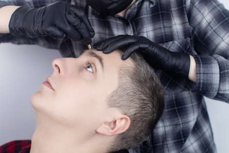 Close-up of a barber shop, in which a specialist plucking eyebrows. Male beauty salon. Hair care. Professional correction of thick eyebrows. Barbershop conceptの写真素材