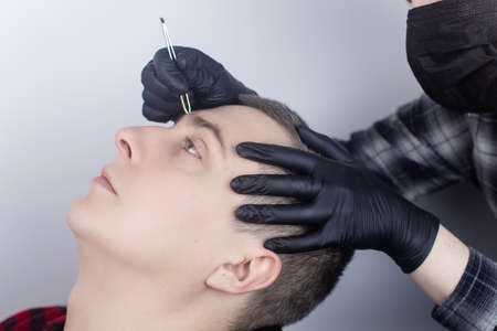 Close-up of a barber shop, in which a specialist plucking eyebrows. Male beauty salon. Hair care. Professional correction of thick eyebrows. Barbershop conceptの写真素材
