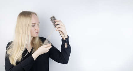Close-up of a girl whose hair is falling out. There is a large tuft of tangled curls on the comb. The blonde looks upset into the frame. The concept of women problems with the scalpの写真素材