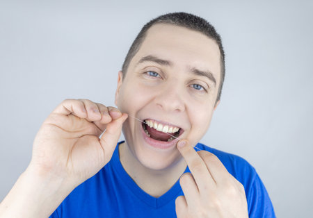 Dental floss close up. A man in front of a mirror brushes his teeth with flossing. The concept of proper oral care. selective focus.の写真素材