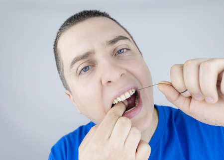 Dental floss close up. A man in front of a mirror brushes his teeth with flossing. The concept of proper oral care. selective focus.の写真素材