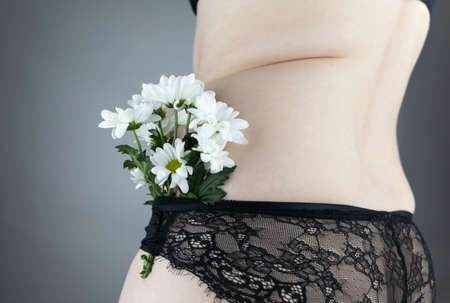 Close-up girl from behind. Side Pleats. Excess weight. Adoption non-ideal figure. Body positivity among women. concept shot. Flowers protrude from underpants, symbolizing acceptance one's appearance.の写真素材