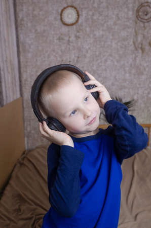 Boy in headphones listens to a meditation for children before going to bed. Concept of a healthy nervous system of children. Relaxation before sleep. Blond guy is relaxing at home. Hearing therapyの写真素材
