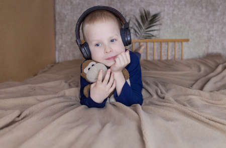 Boy in headphones listens to a meditation for children before going to bed. Concept of a healthy nervous system of children. Relaxation before sleep. Blond guy is relaxing at home. Hearing therapyの写真素材
