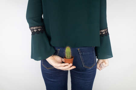 concept. A woman holds a cactus as a symbol of rectal pain. Varicose veins of the lower intestine. Pain in the rectum, hemorrhoids and pain in the excretory system of the body. Proctologyの写真素材