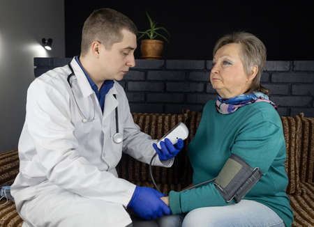 Cardiologist doctor measures blood pressure of a senior woman. Device for self-diagnosis and control of the heart. High or low pressure. Hypertension or hypotension. concept of cardiovascular diseaseの写真素材