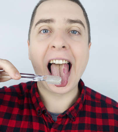 Clean tongue. Close-up of a man performing antimicrobial hygiene with a special tongue brush. isolated on white background. Male looks into the frame, as if he is looking in a mirror. white coatingの写真素材
