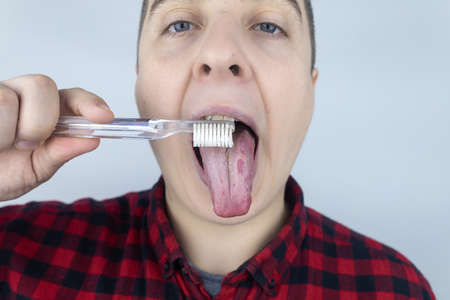 Clean tongue. Close-up of a man performing antimicrobial hygiene with a special tongue brush. isolated on white background. Male looks into the frame, as if he is looking in a mirror. white coatingの写真素材