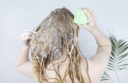 Solid hair shampoo. Close-up of a blonde girl in the bathroom, which lathers her hair with dry shampoo. Lots of foam and peek effect.の写真素材