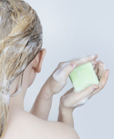 Solid hair shampoo. Close-up of a blonde girl in the bathroom, which lathers her hair with dry shampoo. Lots of foam and peek effect.の写真素材