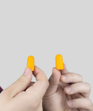 The man puts on earplugs. Close-up of an orange noise barrier. deep sleep. The ENT doctor advises orange earmuffs to reduce ambient noise. Increased sensitivity to sounds.の写真素材