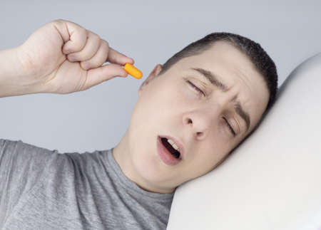 The man puts on earplugs. Close-up of an orange noise barrier. deep sleep. The ENT doctor advises orange earmuffs to reduce ambient noise. Increased sensitivity to sounds.の写真素材
