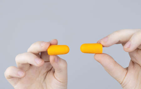 The man puts on earplugs. Close-up of an orange noise barrier. deep sleep. The ENT doctor advises orange earmuffs to reduce ambient noise. Increased sensitivity to sounds.の写真素材