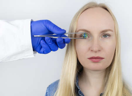 Conceptual shot of an eye crystalline lens replacement. Ophthalmic surgery. Return of sight. Removal of cataracts. Surgical intervention in the eyeball. Doctor holds the implant near the patientの写真素材