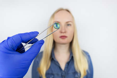 Conceptual shot of an eye crystalline lens replacement. Ophthalmic surgery. Return of sight. Removal of cataracts. Surgical intervention in the eyeball. Doctor holds the implant near the patientの写真素材
